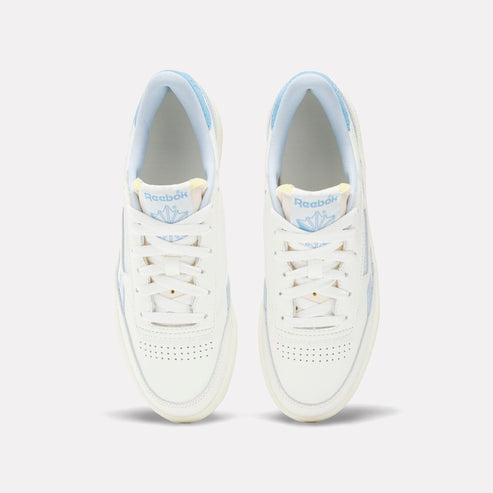 Overhead view of two white leather sneakers with white laces and light blue accents on the heel and tongue lining.