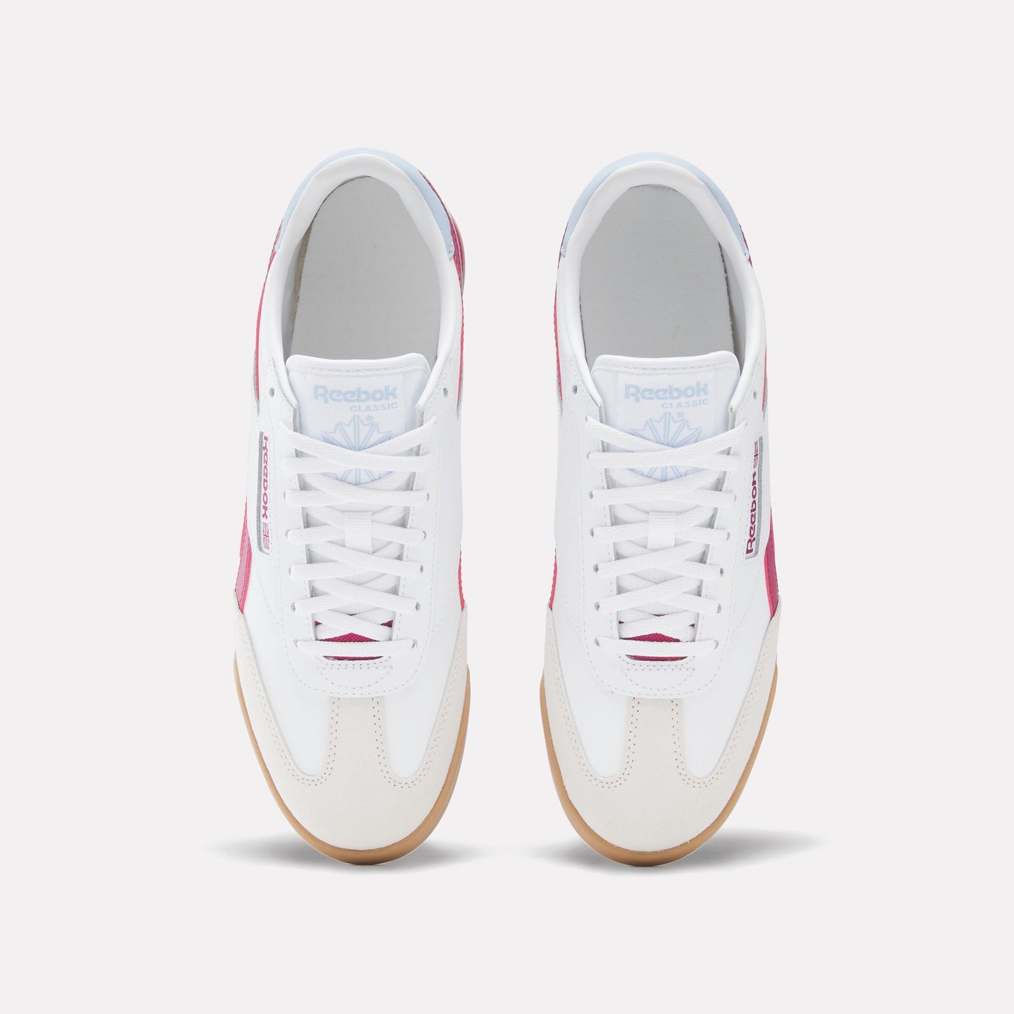 Top-down view of white sneakers with white laces, a gum sole, and pink accents, featuring the text "Reebok CLASSIC".