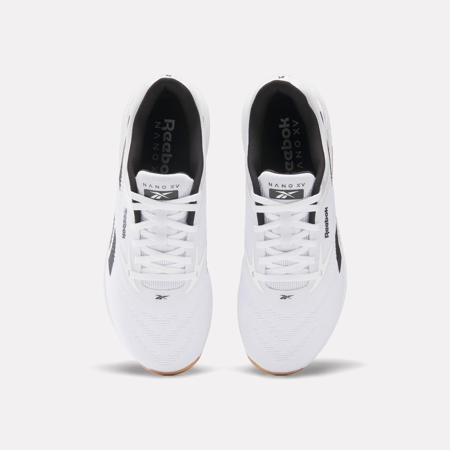 Overhead view of two white athletic shoes with white laces and black interior lining. Text "Reebok Nano XV" is visible on the tongue of the shoe. 