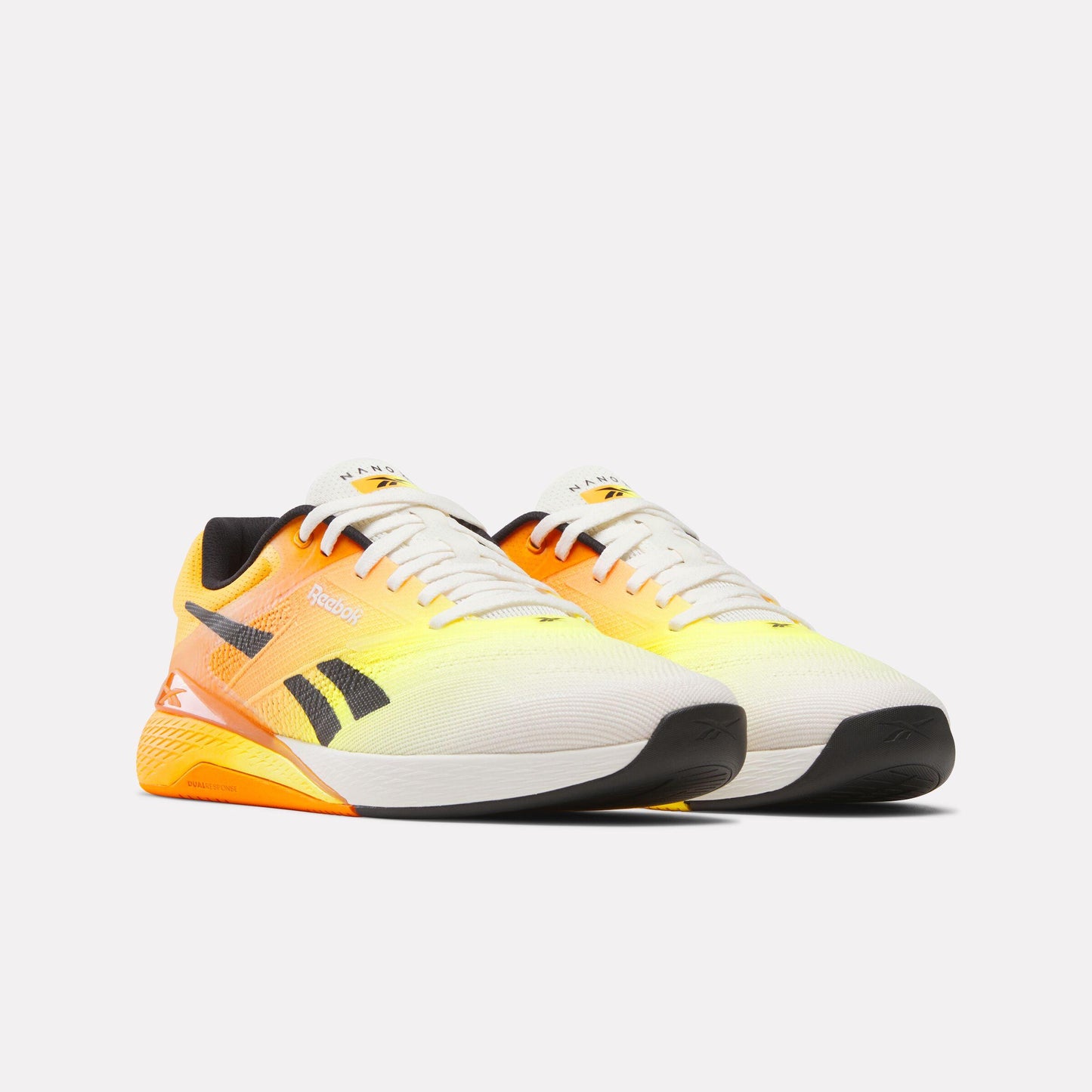Pair of athletic shoes fading from black sole and white toe into a bright yellow and orange heel with a black logo.