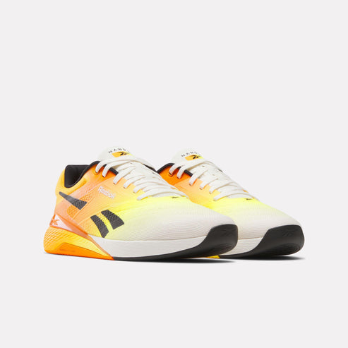 Pair of athletic shoes fading from black sole and white toe into a bright yellow and orange heel with a black logo.