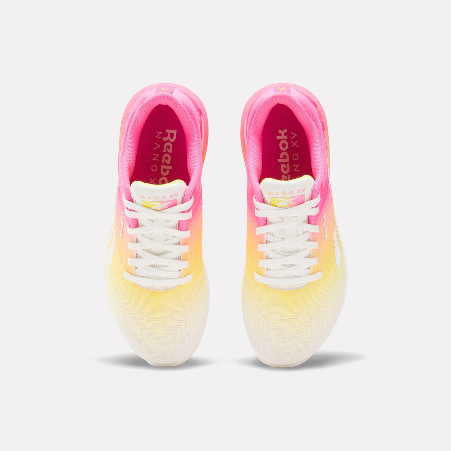 Top-down view of pink, orange, and yellow gradient athletic shoes with white laces; visible Reebok text on the tongue.