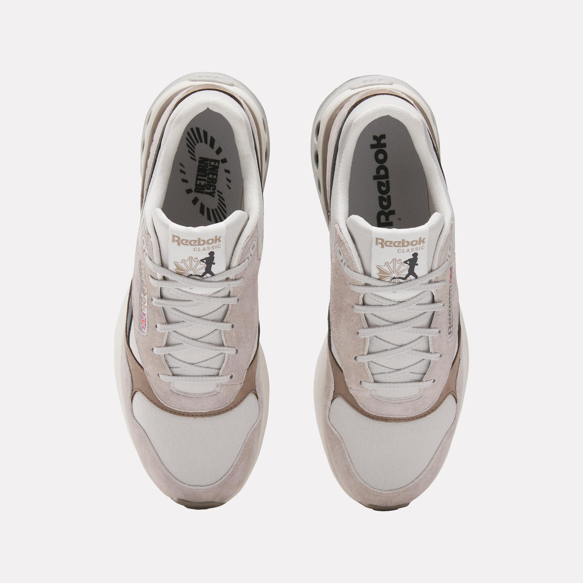 Top-down view of two matching sneakers with off-white suede and textile uppers, white laces, brown accent panels, and white interiors displaying visible 'Reebok' text.