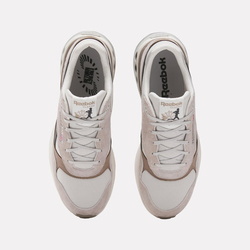Top-down view of two matching sneakers with off-white suede and textile uppers, white laces, brown accent panels, and white interiors displaying visible 'Reebok' text.