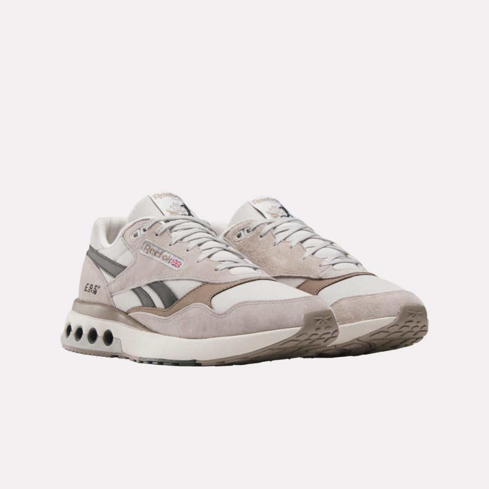 Two off-white sneakers with grey and brown accents, displaying text Reebok.