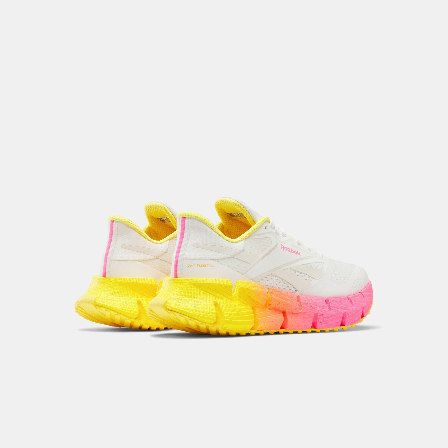 Pair of low-rise athletic shoes with white tops, neon yellow midsoles that fade to neon pink.