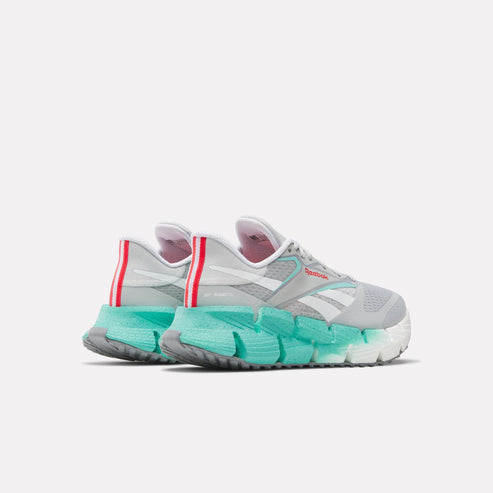 Rear view of gray and white sneakers with thick, teal-colored, zigzag soles and red stripes on the heels.