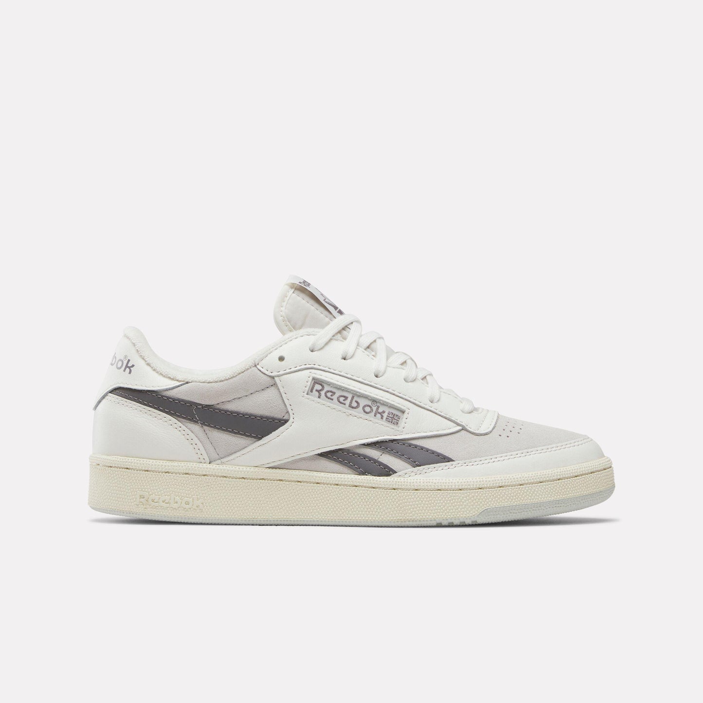 Low-top off-white sneaker with grey stripe and cream-colored sole. The word "Reebok" is on the side.