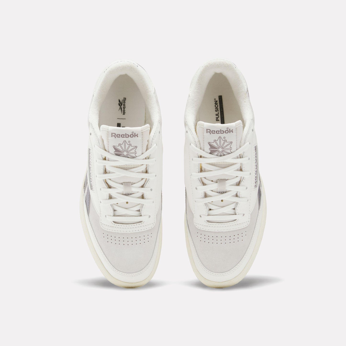 Two white sneakers facing forward, with white laces and a logo on the tongue.