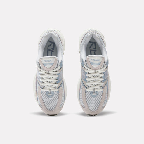 Top-down view of two identical white running shoes with white laces and grey accents, with "RBK" printed on the tongue.