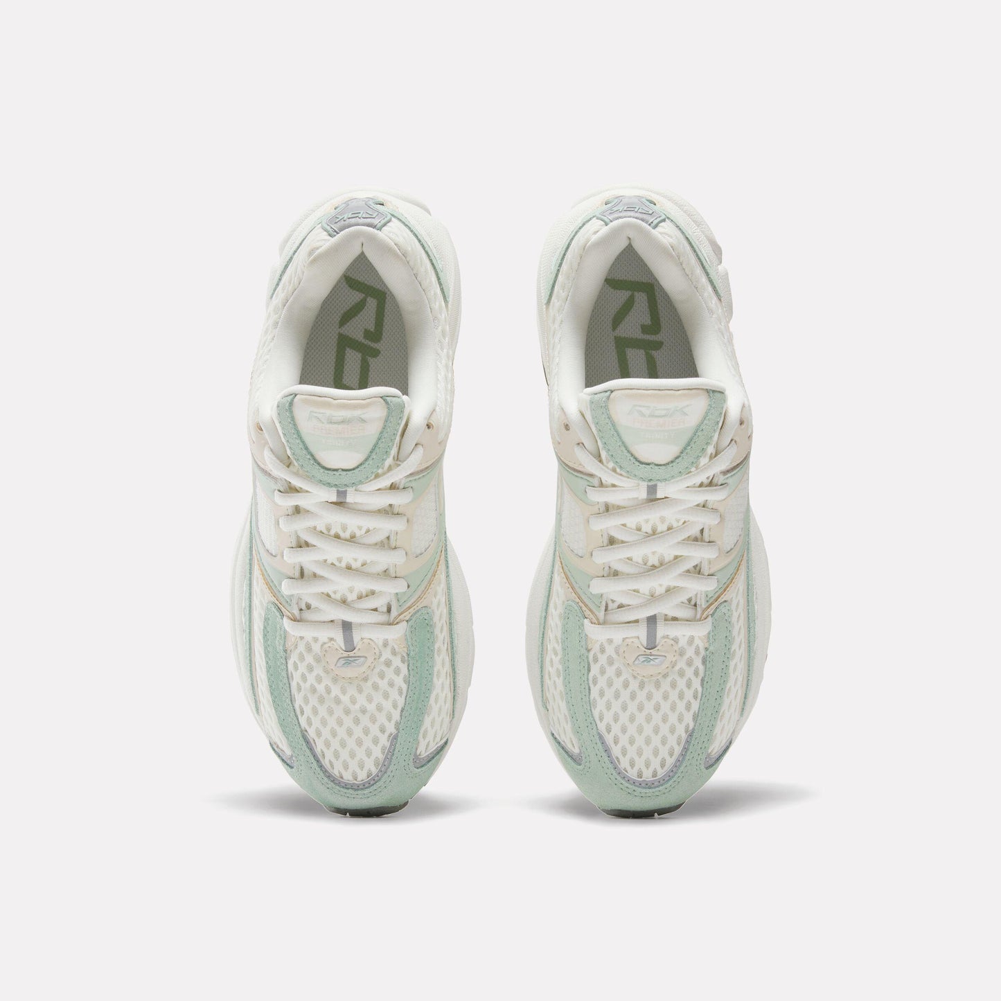 Pair of off-white sneakers with white laces and light green accents. The letters "RBK" are visible inside the shoe.