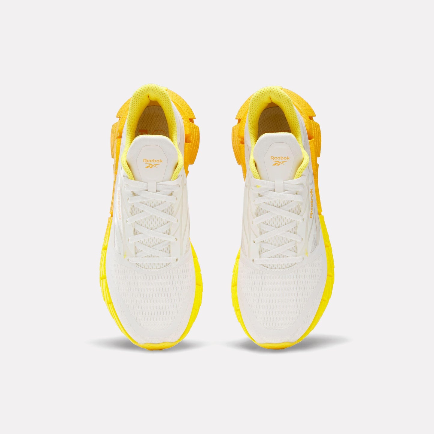 Pair of white and yellow sneakers with a lace-up closure and a unique geometric pattern on the sole.