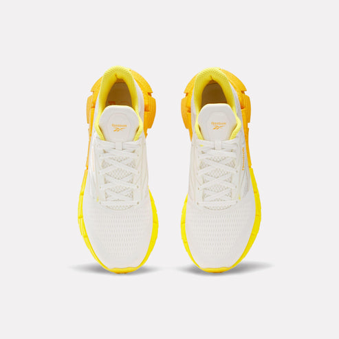Pair of white and yellow sneakers with a lace-up closure and a unique geometric pattern on the sole.