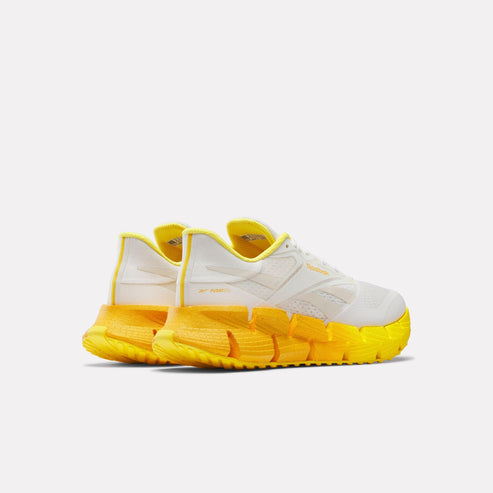 Rear view of white shoes with thick yellow zigzag sole.