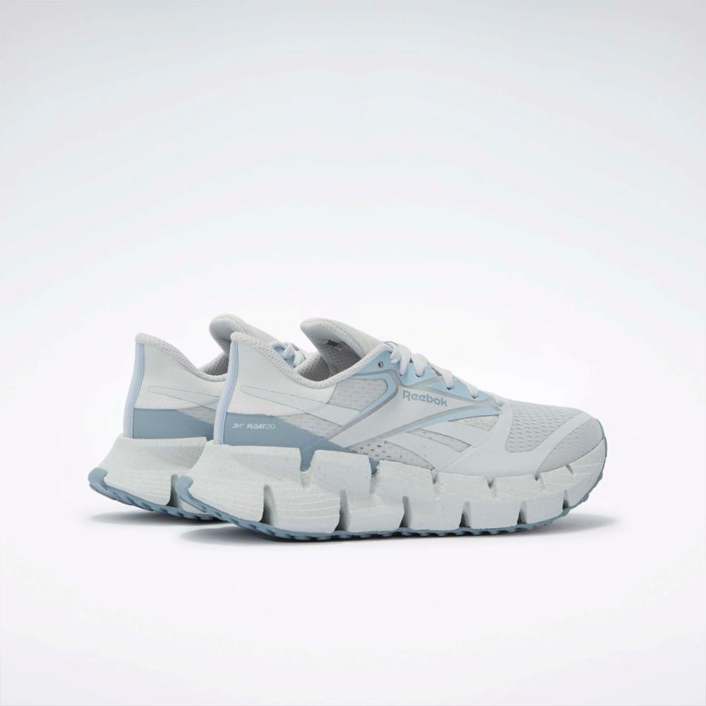 A pair of white athletic shoes with light blue accents have a textured zigzag sole.
