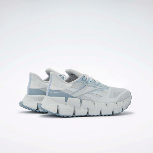 A pair of white athletic shoes with light blue accents have a textured zigzag sole.