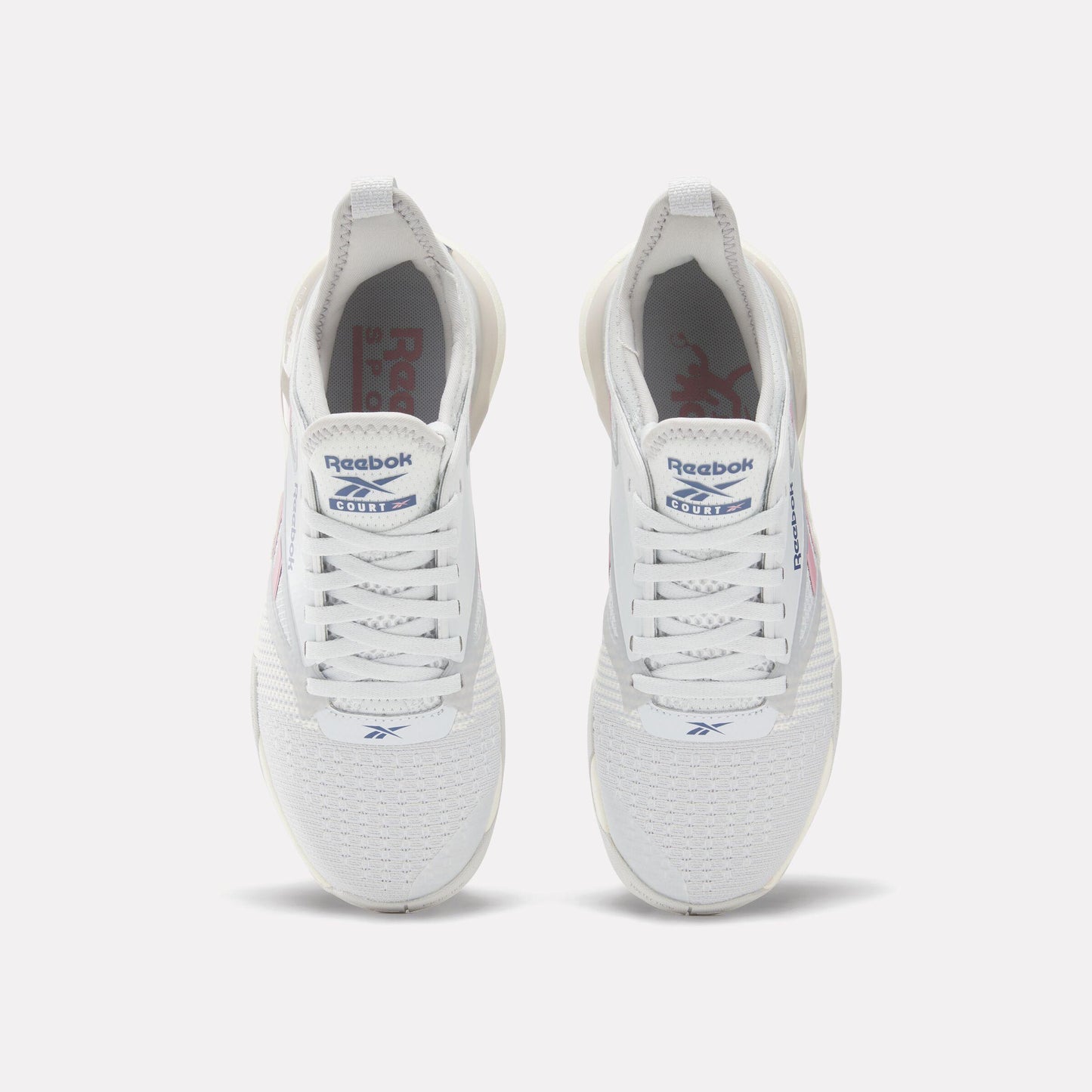 Pair of white athletic shoes, seen from above, with white laces, “Reebok” and an abstract logo visible on the tongue.