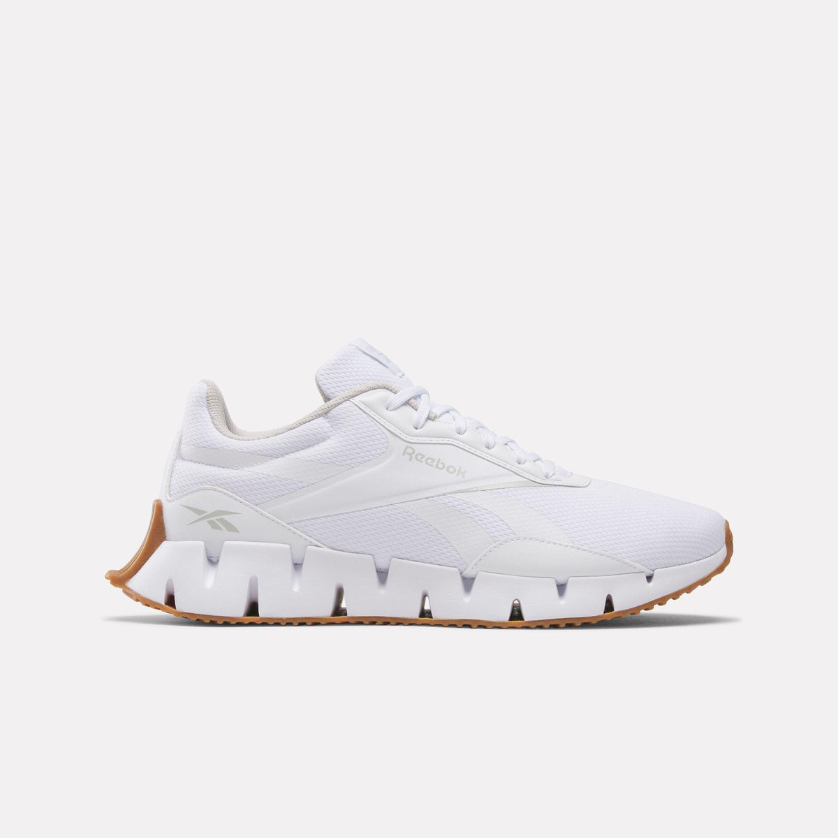 A white athletic shoe featuring the text 'Reebok' in a small font on the side, with a unique zig-zag patterned white midsole and a gum-colored outsole.