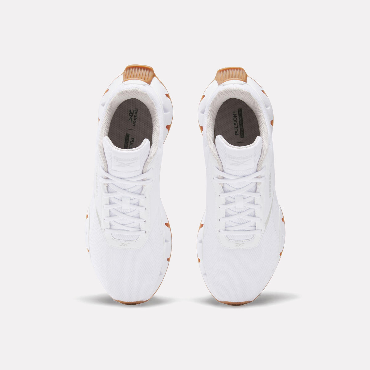 Overhead view of two identical white leather sneakers with brown accents and white laces.