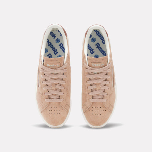 Top-down view of two peach-colored sneakers with white soles and white interior fabric featuring blue text.