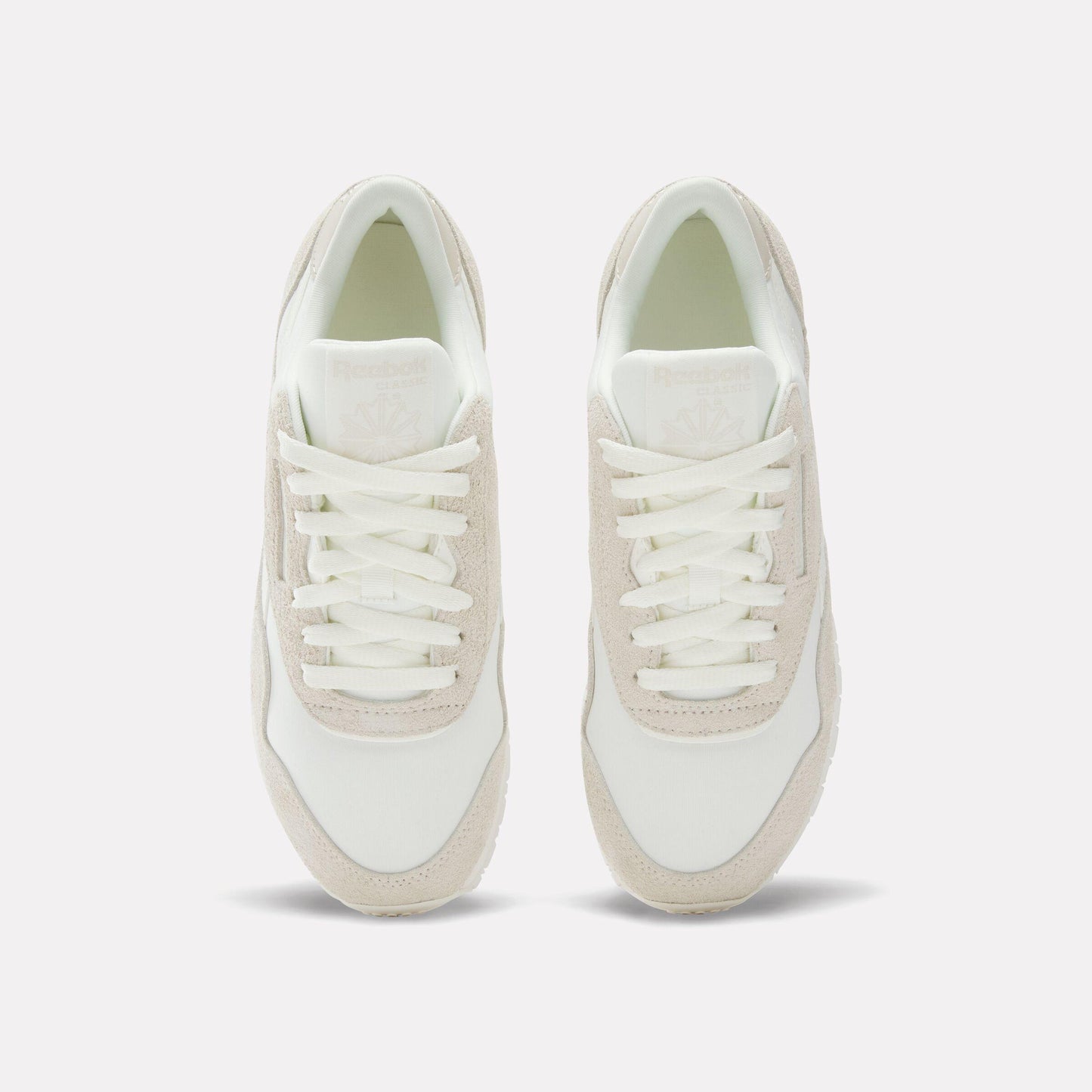 A pair of running shoes, seen from above, that are cream and white with white laces.