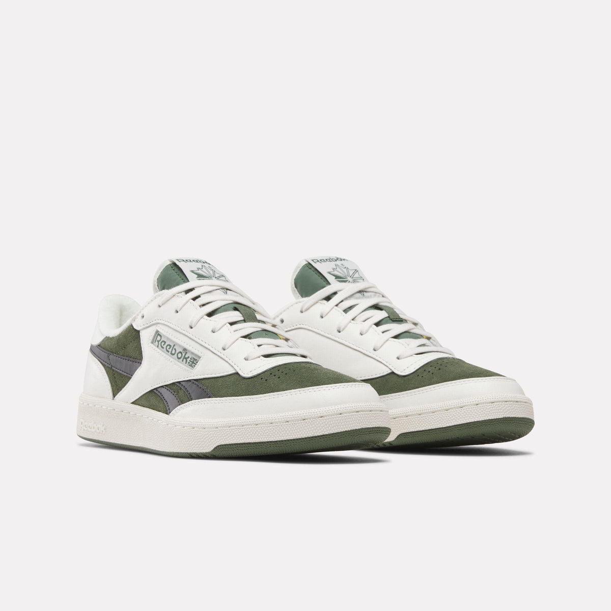 Pair of low-top white and green sneakers with white laces and white outsoles, with a gray Reebok logo on the side.