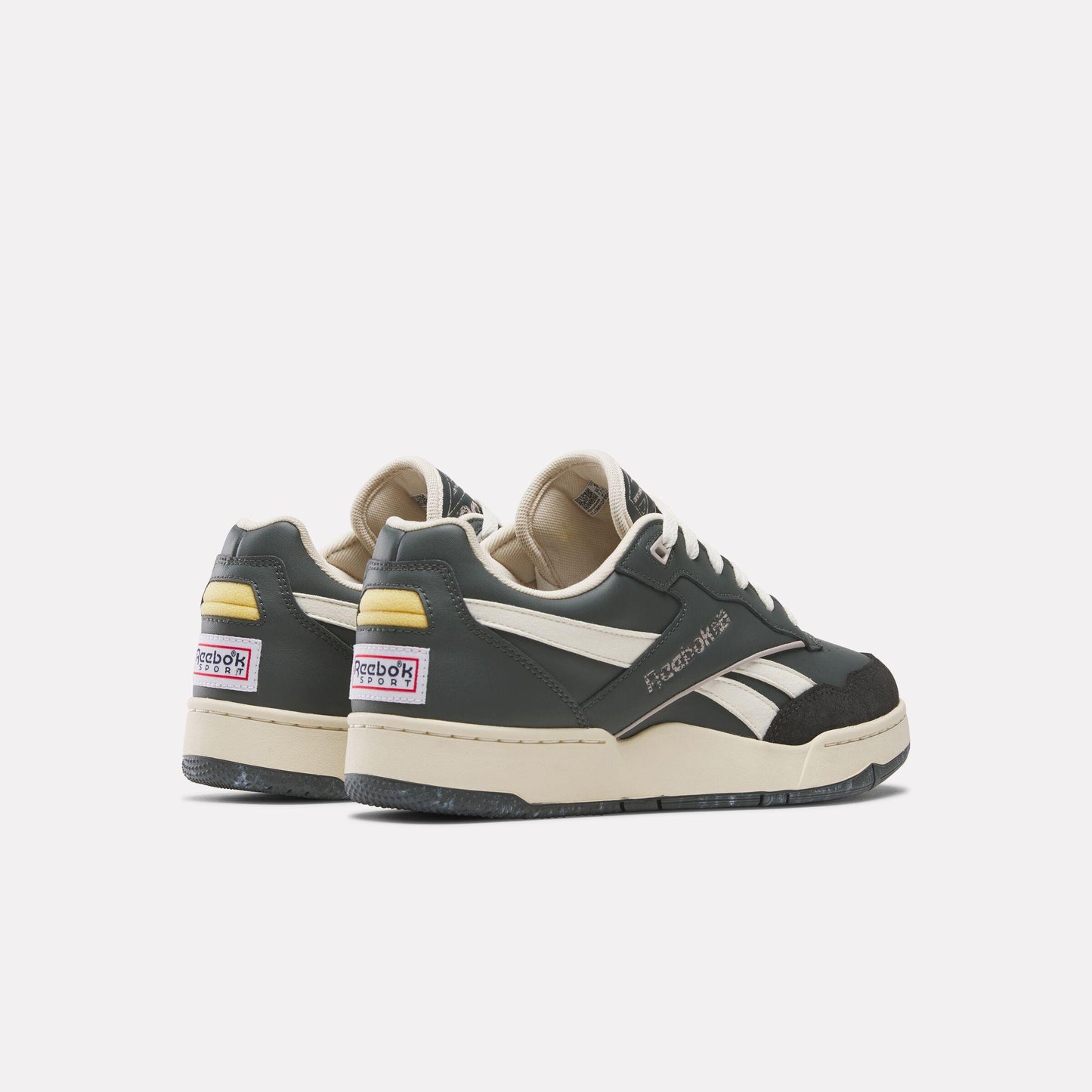 Two Reebok Court Advance sneakers viewed from the back, black and white with cream sole and yellow accents on the heel, Reebok label.