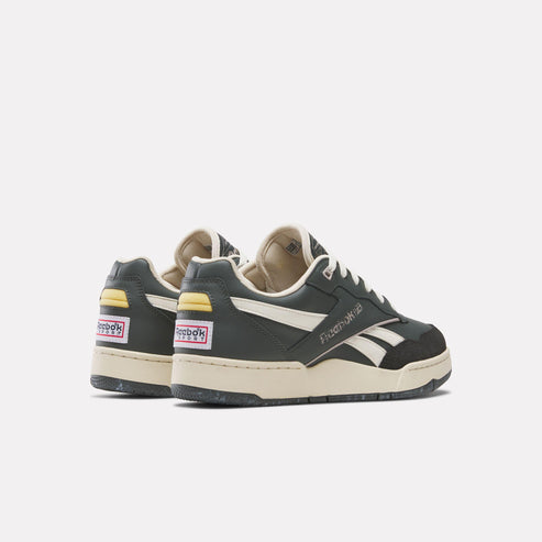 Two Reebok Court Advance sneakers viewed from the back, black and white with cream sole and yellow accents on the heel, Reebok label.