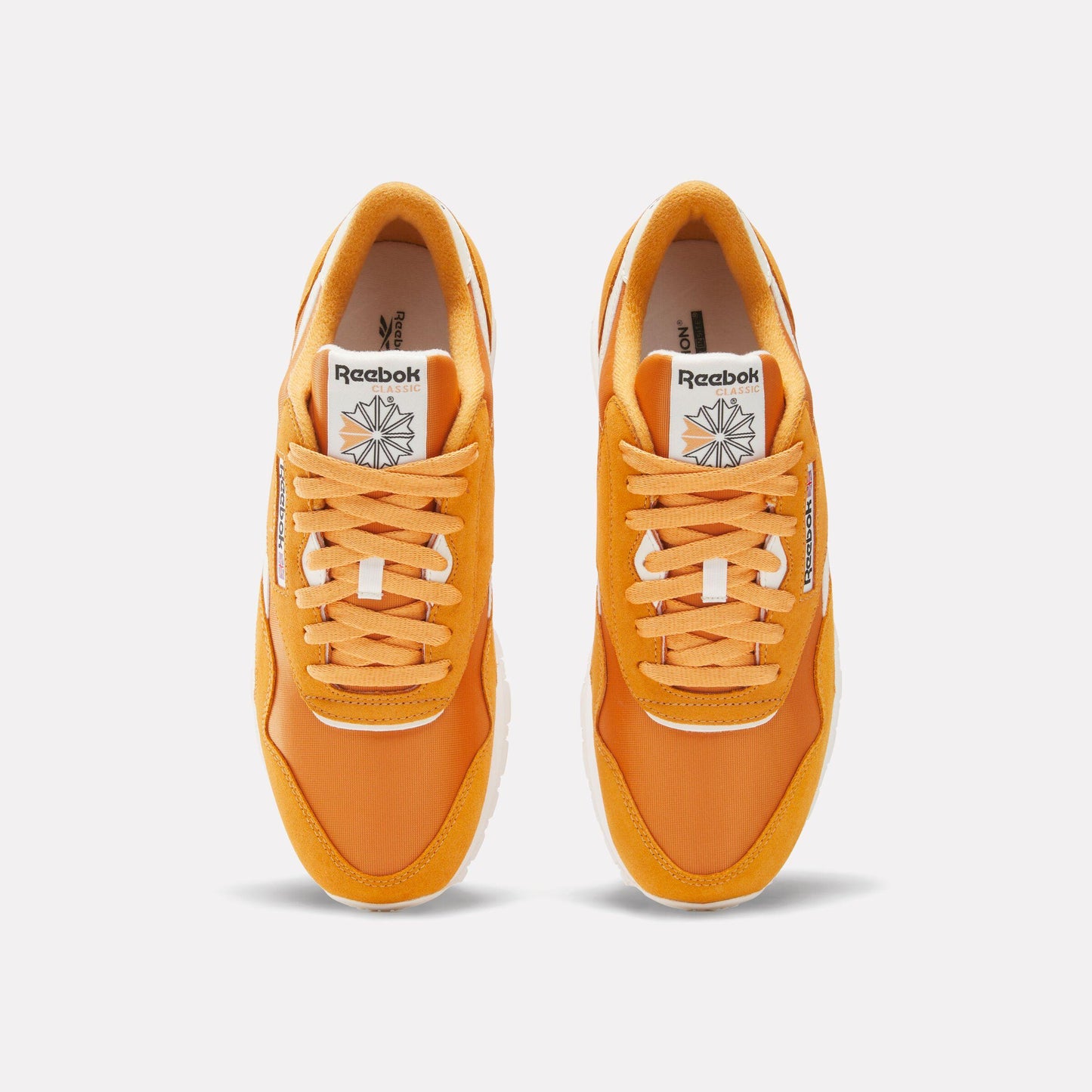 A pair of orange sneakers with white laces and a white logo on the tongue.