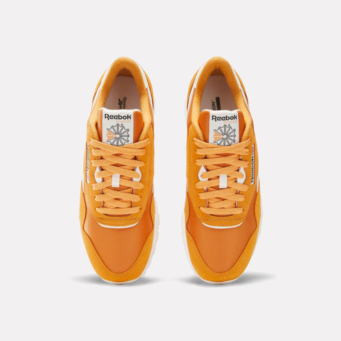 A pair of orange sneakers with white laces and a white logo on the tongue.