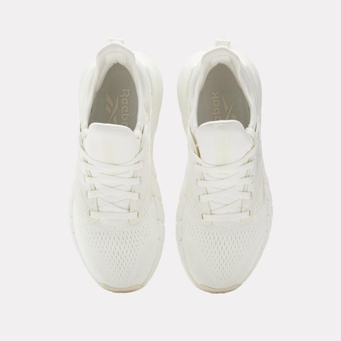 Pair of white sneakers, viewed from above, with white laces and a visible logo on the inner side.