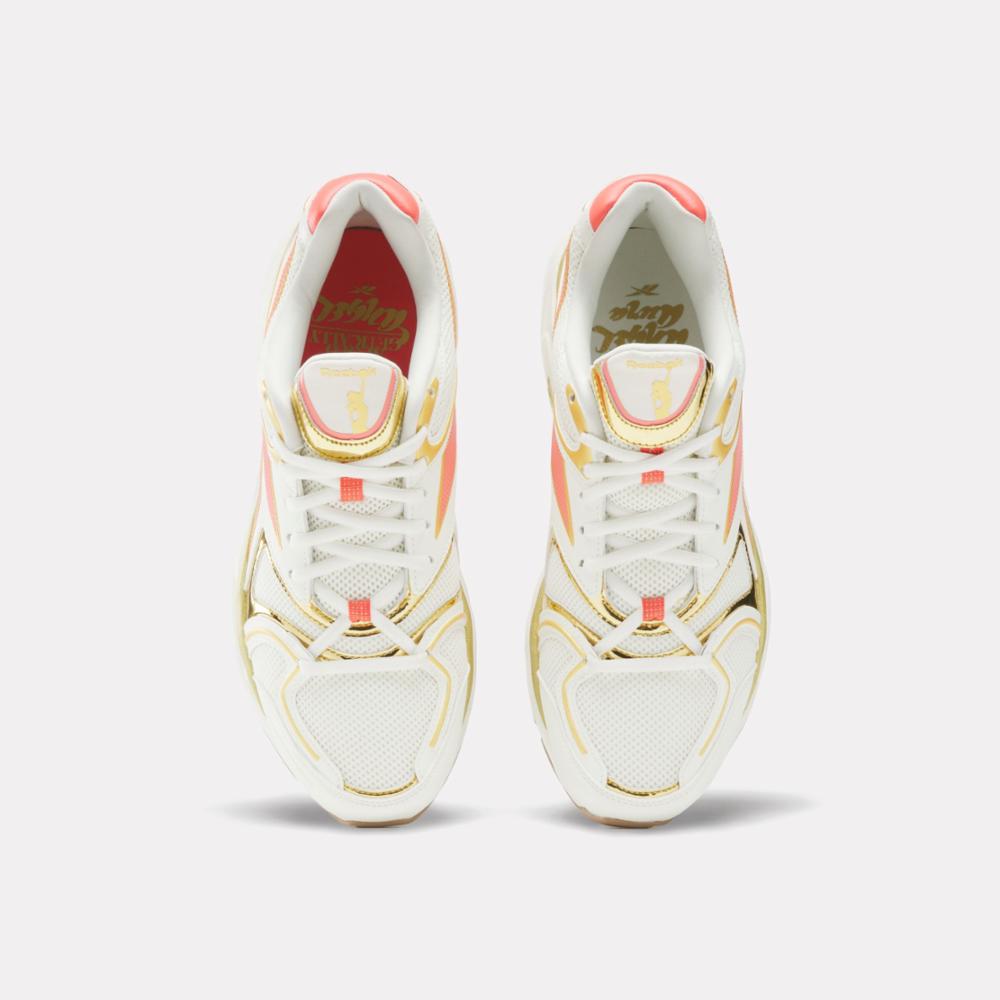 A pair of white running shoes with gold accents and coral details. They have white laces and mesh on the front.