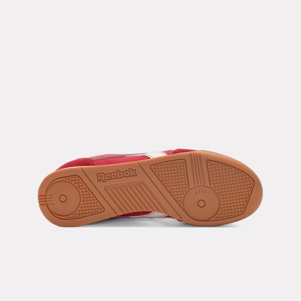 Close up of the underside of a red tennis shoe, showing a brown rubber sole with repeating ridges and circular textured designs.