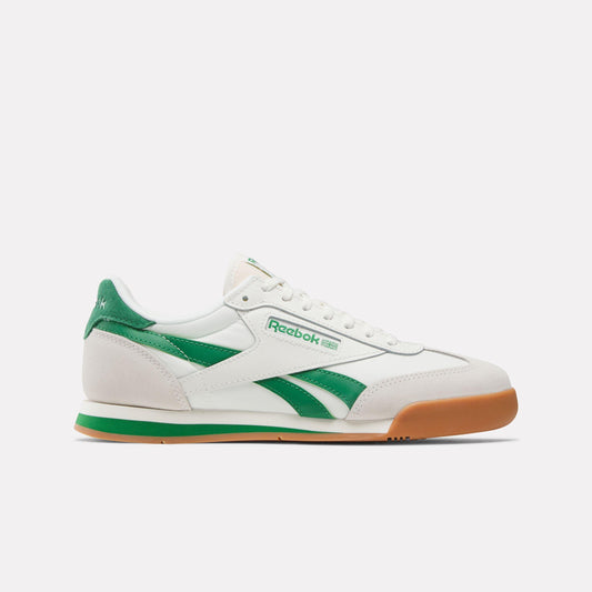 A white sneaker with green accents, a brown toe, and the word "Reebok" printed on the side.