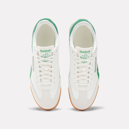 A pair of off-white sneakers with white laces and a gum sole, featuring green accents around the heel, tongue, and side with "Reebok CLASSIC" imprinted.
