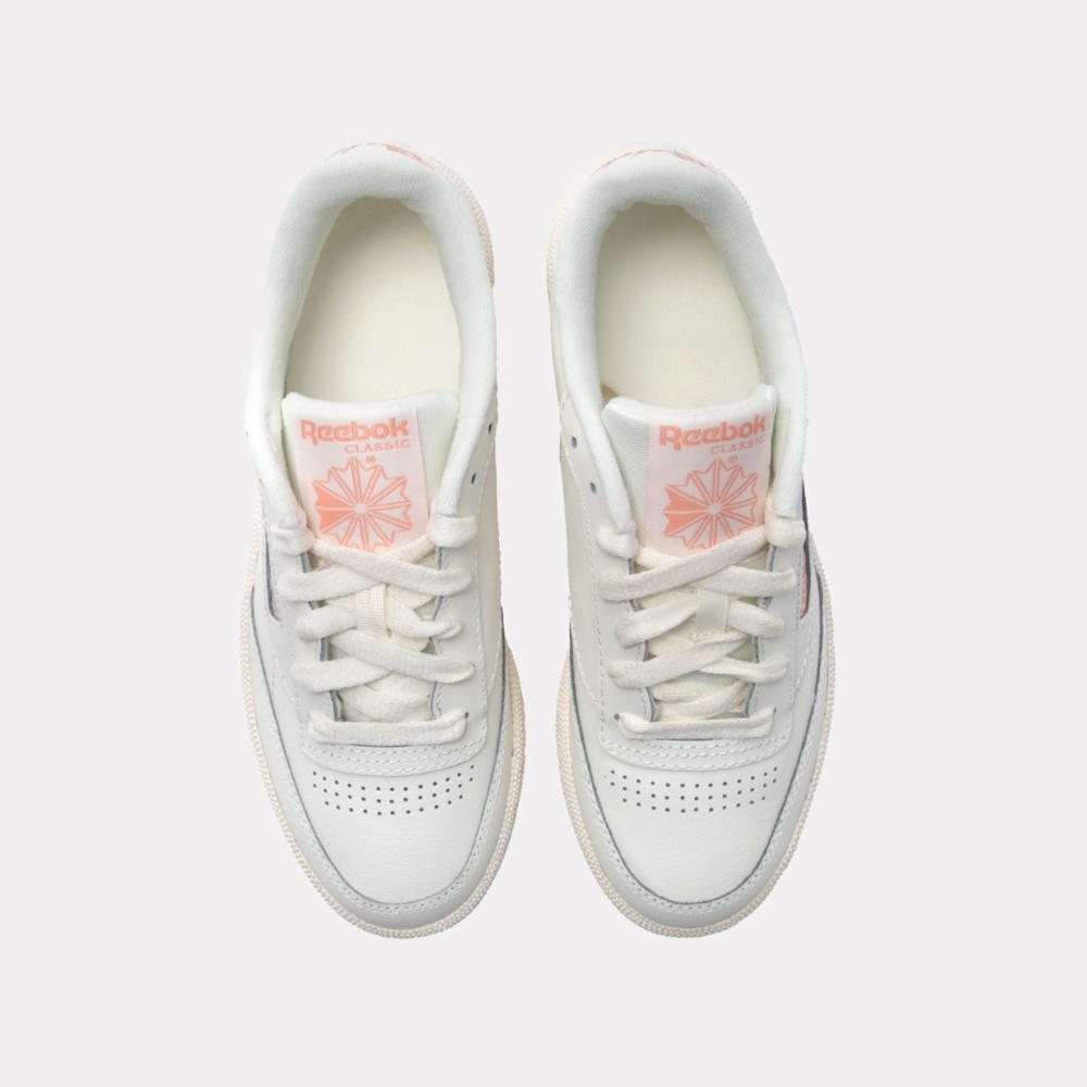 Pair of white sneakers with pink logo and white laces.