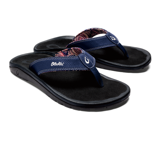 A pair of navy blue flip-flops with paisley print on straps and white text 'Olukai' on the side.