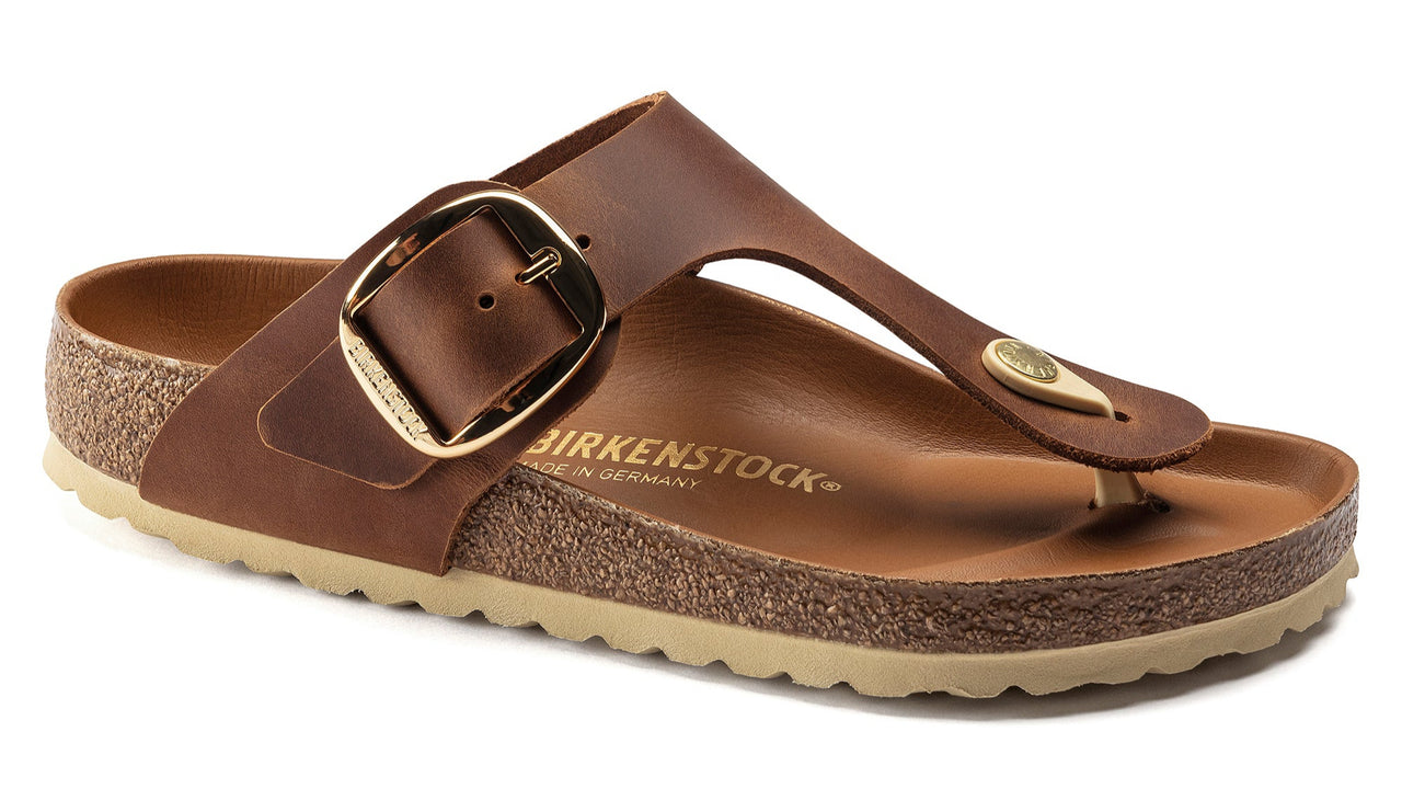 Brown sandal with a large gold buckle and a toe loop.