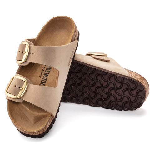 Two tan leather sandals with large gold buckles on a cork sole.