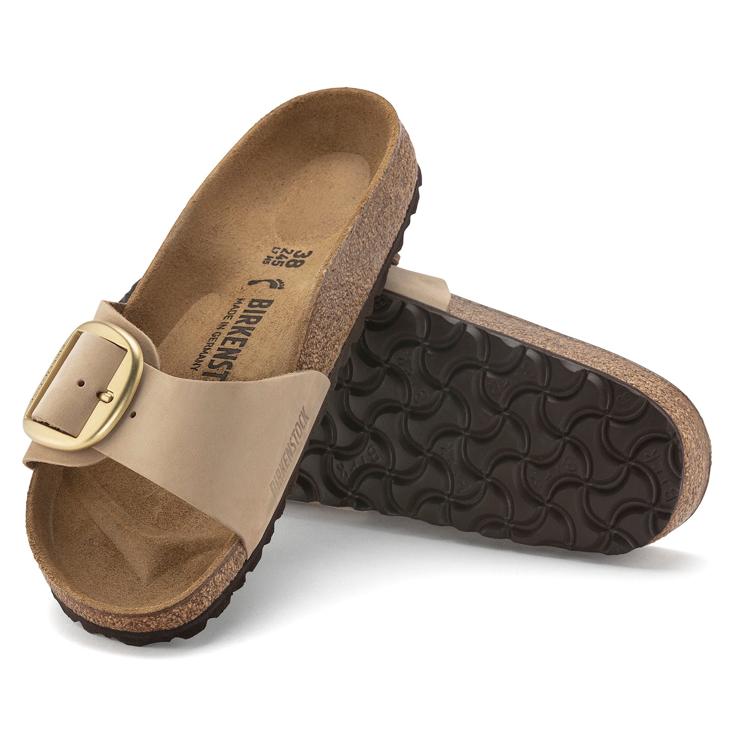 Two Birkenstock sandals, one upright and the other on its side, are shown with light brown footbeds and straps, and oversized brass colored buckles; the sole of the sideways sandal is visible and has a diamond patterned tread.