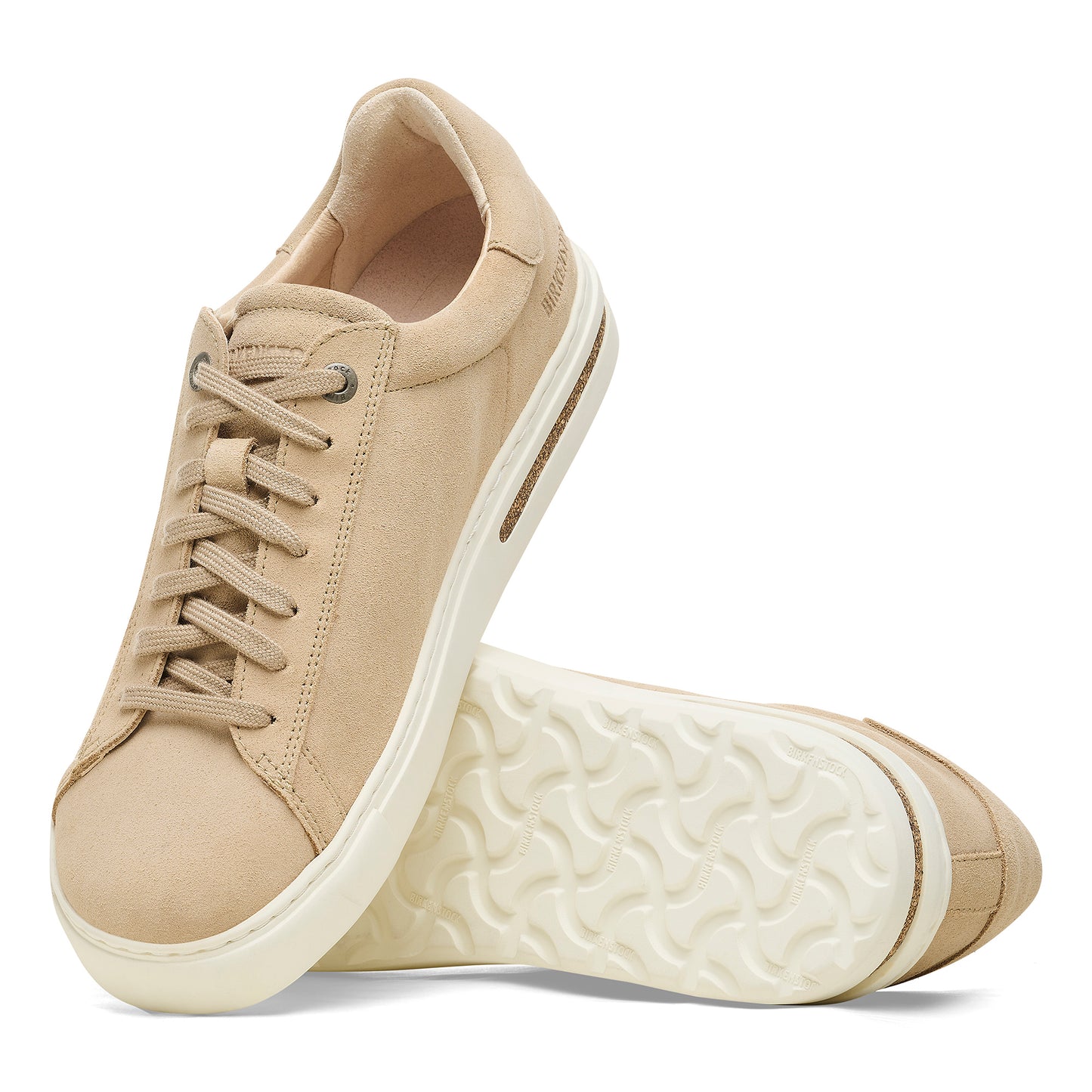 A pair of beige-colored, laced sneakers. One shoe is upright and angled, while the other is lying on its sole.