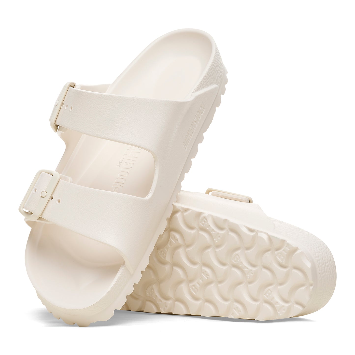 Pair of white two-strap slide sandals with buckles, soles facing the viewer.
