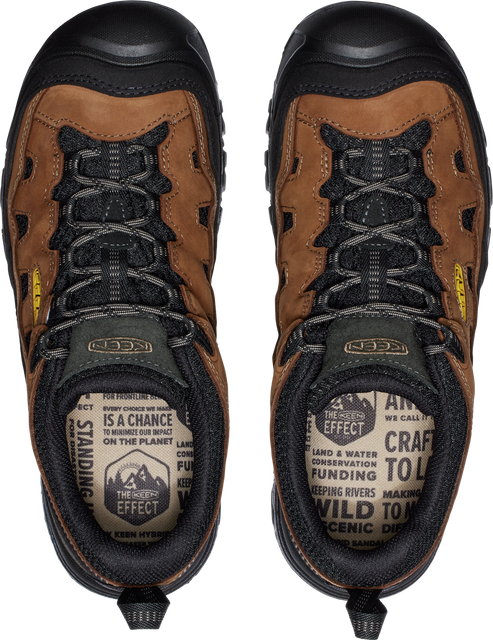 A top-down view of two brown hiking boots. The tongues have black laces and the insole is patterned with text: "Every choice we make is a chance to minimize our impact on the planet. The Scenic Effect, land & water, conservation funding, keeping rivers wild to making scenic dinner."