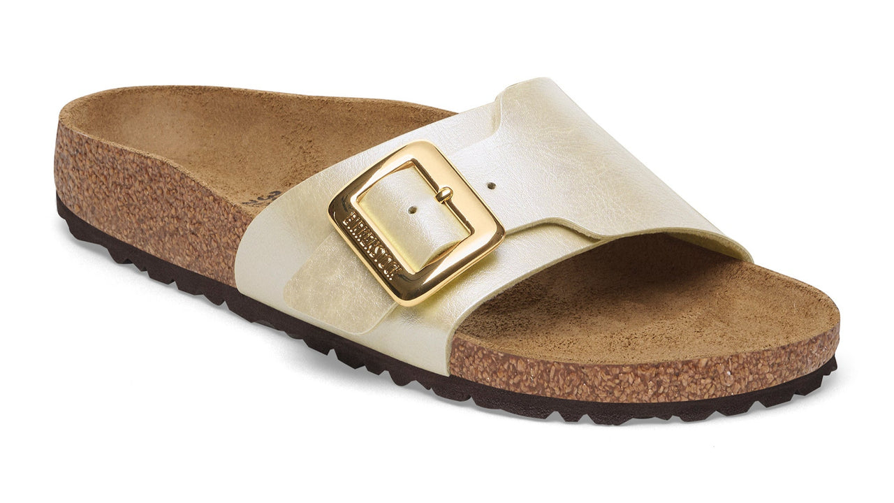 Slide sandal with a pearlescent white strap and a large gold buckle, on a cork footbed with a dark brown sole.