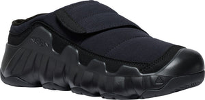 A black slip-on shoe with a thick sole and a velcro strap.