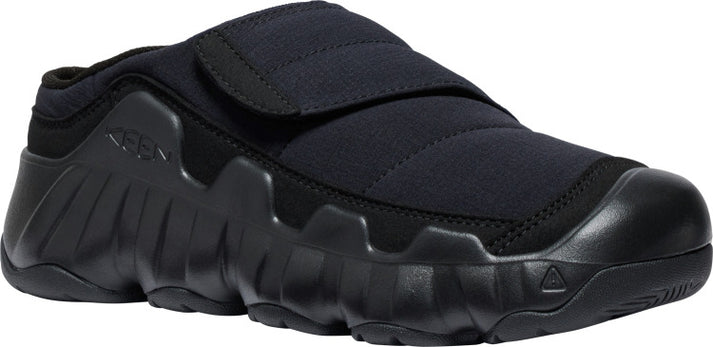 A black slip-on shoe with a thick sole and a velcro strap.
