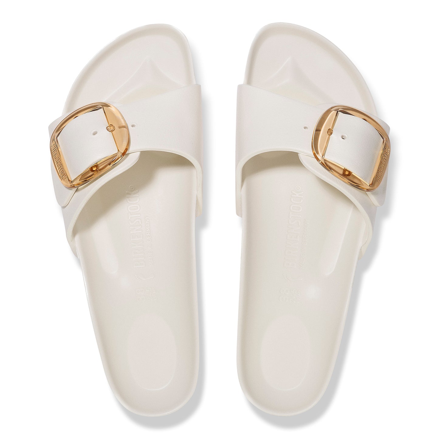 Pair of white slip-on sandals with gold buckle detail.