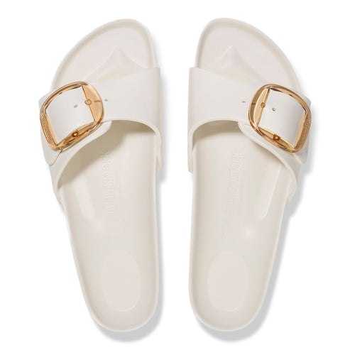 Pair of white slip-on sandals with gold buckle detail.