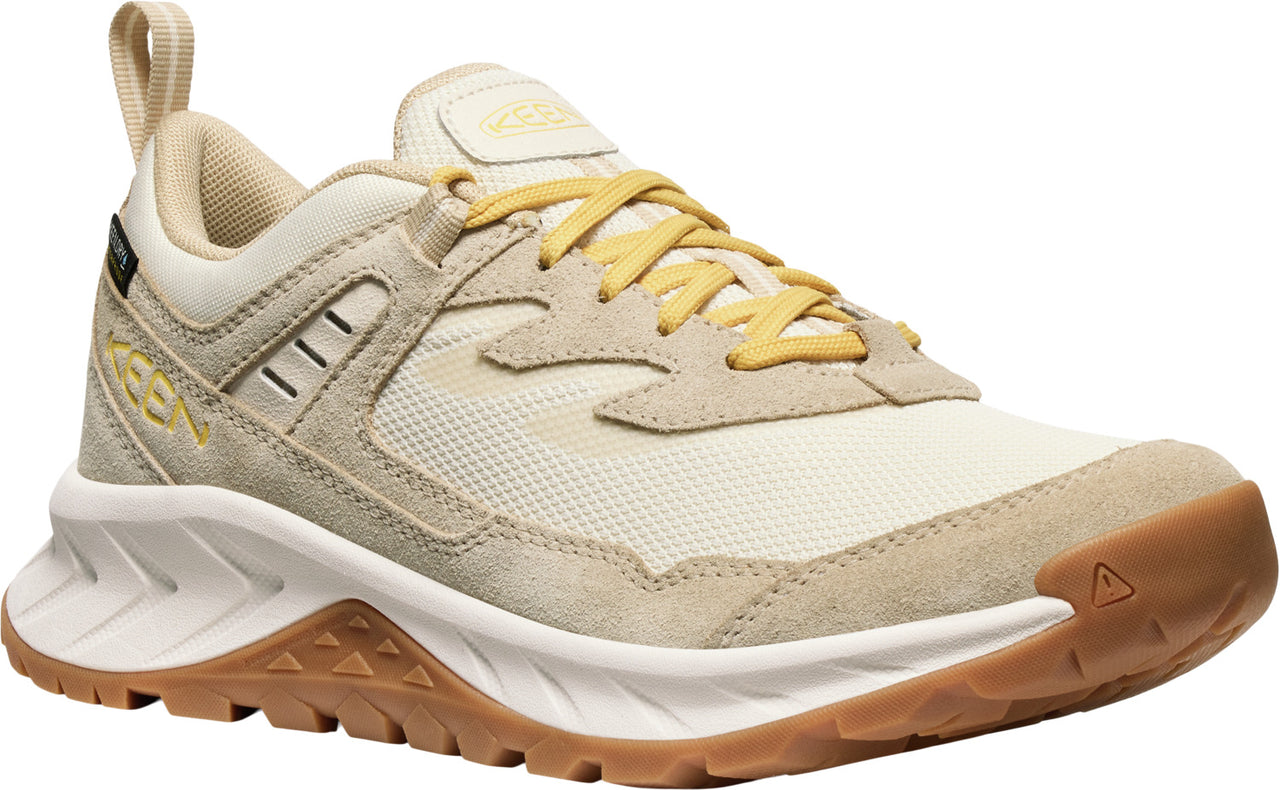 A low-rise athletic shoe featuring beige suede overlays, cream-colored mesh panels, yellow laces, a white midsole, and a brown outsole.