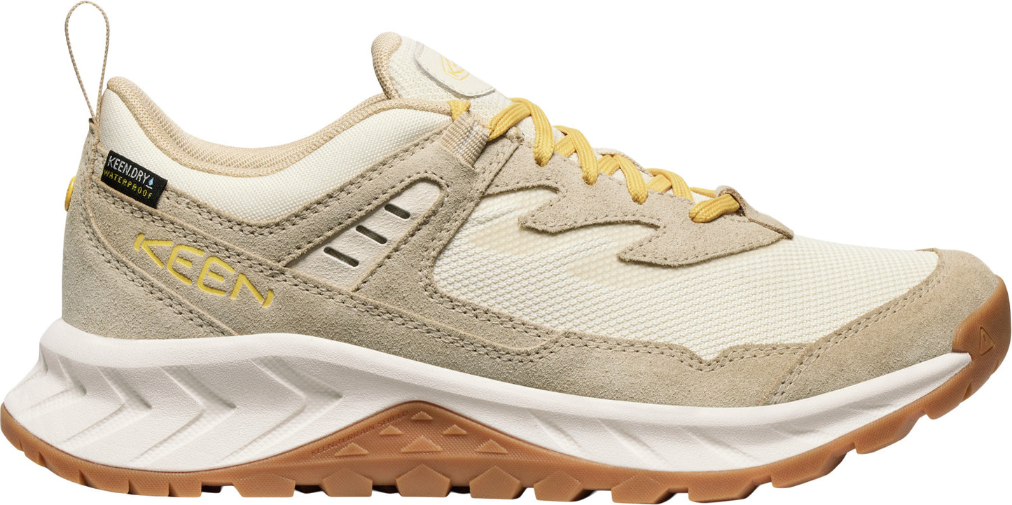 A sneaker with beige suede and white fabric, yellow laces, and white rubber sole with a brown tread.